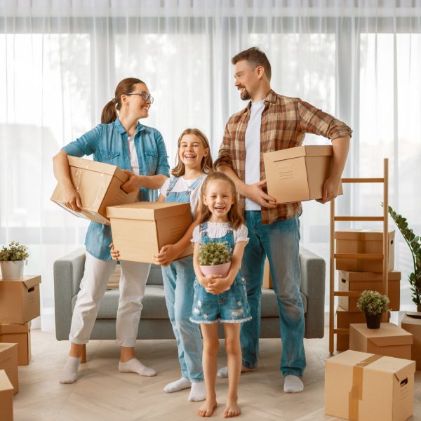 Happy young family are moving to new apartment. Parents and daughters with boxes.